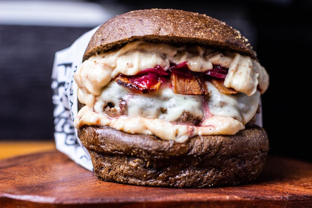 Closeup of appetizing hamburger with cheesy sauce and black bun placed on wooden board in cafe