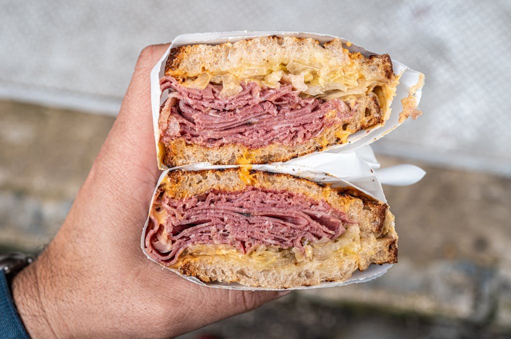 A person holding a sandwich with meat and cheese