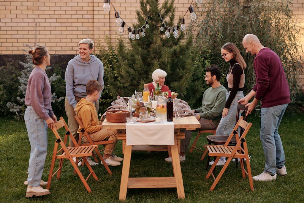 Happy family members talking and sitting down to eat tasty food at big wooden table in backyard in daytime