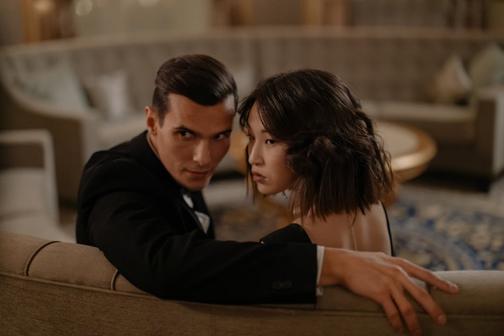 Man in Black Suit Jacket Sitting Beside Woman in Black Dress