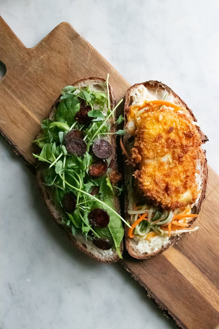 Top view of bruschettas with green rucola and fried chicken breast with vegetables served on wooden cutting board on table