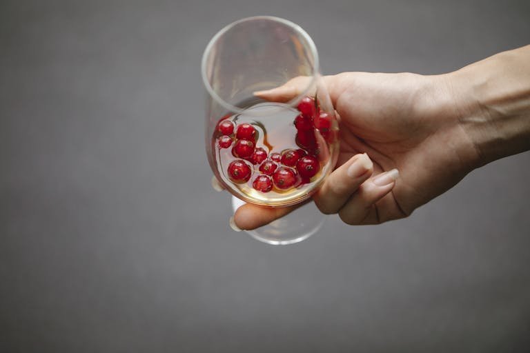 A close-up view of a hand holding a glass with berries and a beverage, emphasizing freshness.