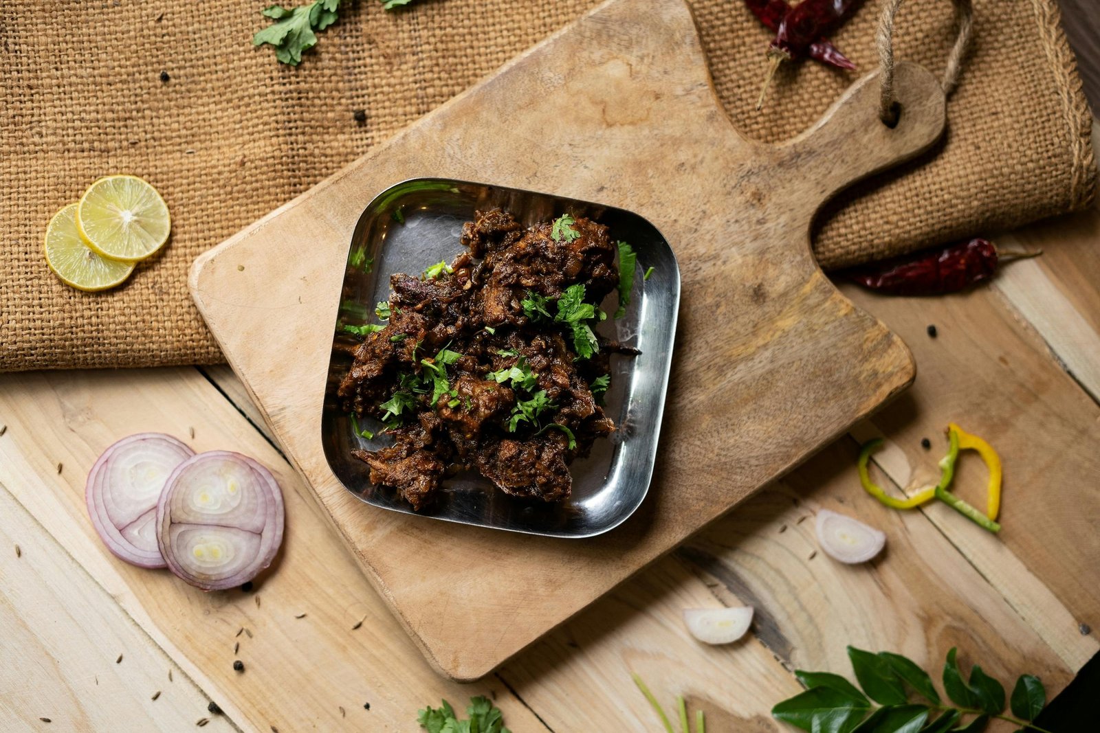 Flat lay of a savory spiced meat dish with herbs on a cutting board, ideal for food lovers.